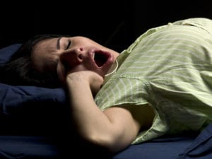 Hispanic young woman sleeping and yawning on black background